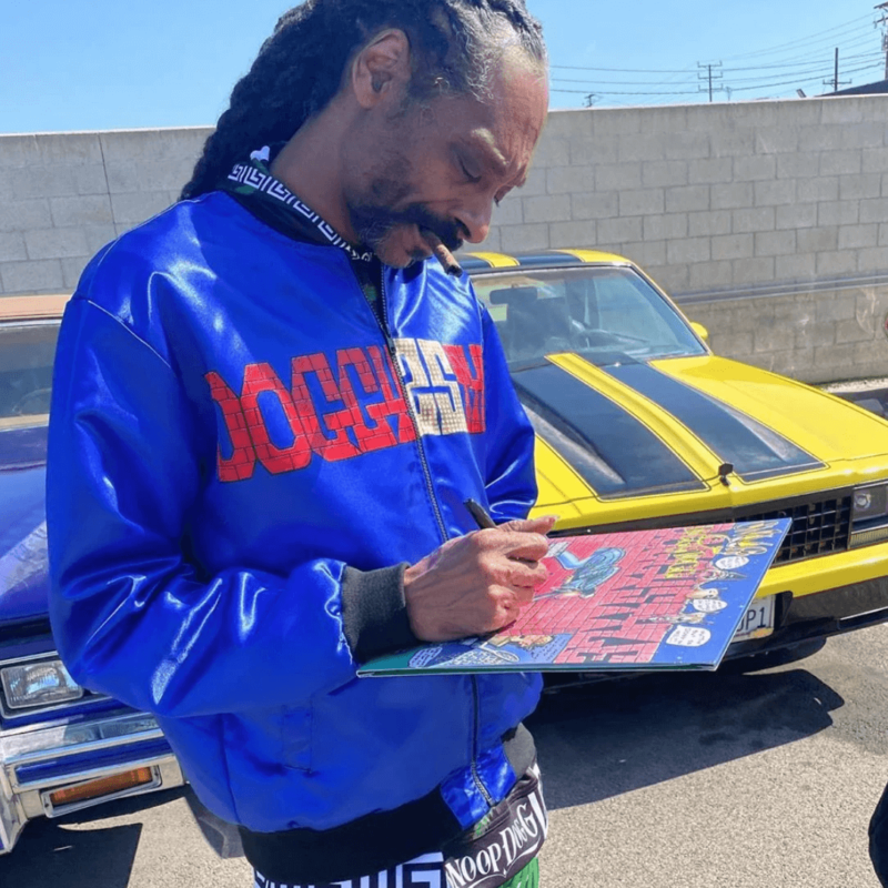 Snoop Dogg giving out autographs while wearing his doggystyle 25th anniversary blue bomber jacket merchandise