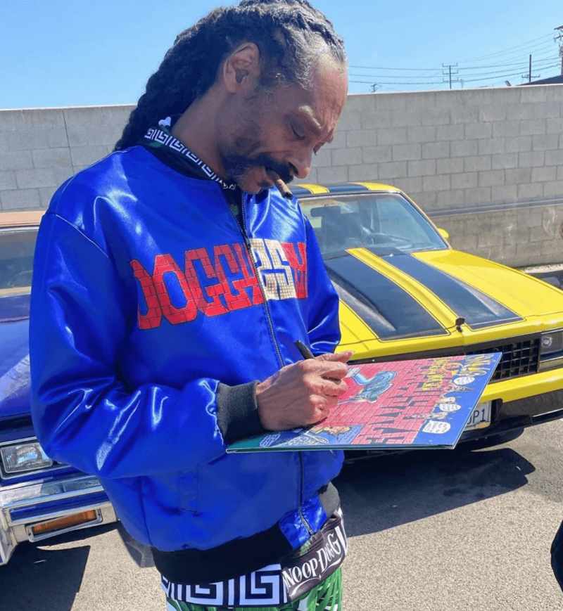 Snoop Dogg giving out autographs while wearing his doggystyle 25th anniversary blue bomber jacket merchandise